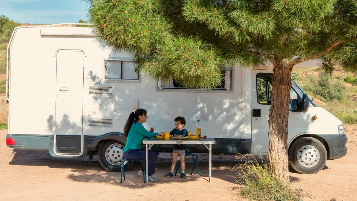 femme-son-fils-table-camping-cote-du-camping-car-ombre-arbre